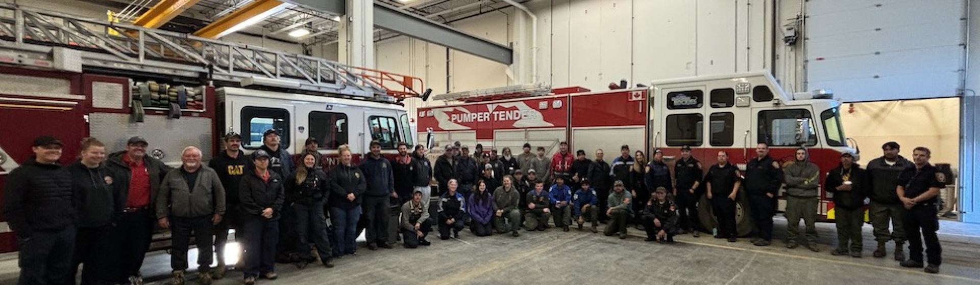 Firefighters posing in front of two fire trucks inside a spacious garage.