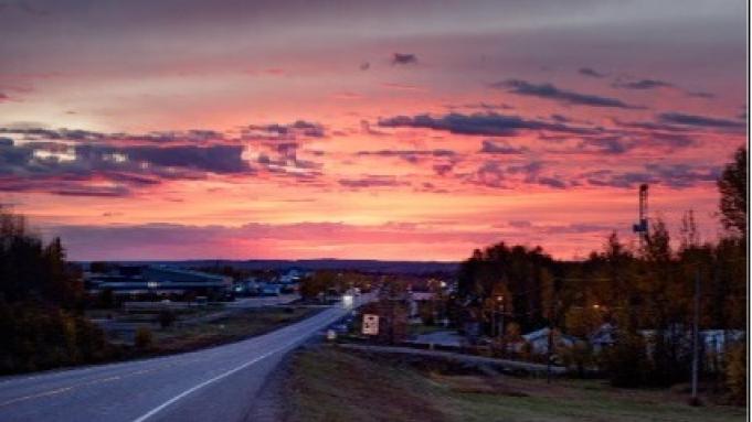 Road leading to a small town under a vibrant pink and purple sunset.