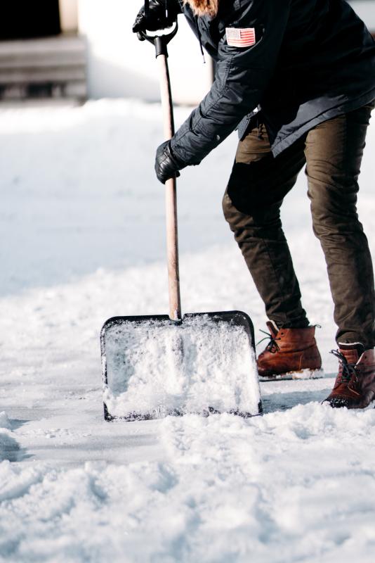 Person shoveling snow outdoors in winter clothing.
