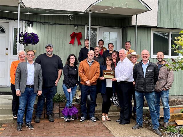 Group of people smiling outside a building with a plaque.