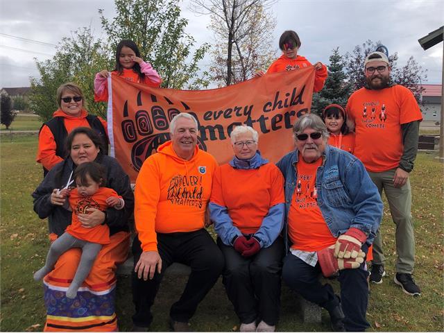 Group of people wearing orange shirts, outdoors on grass with trees in the background.