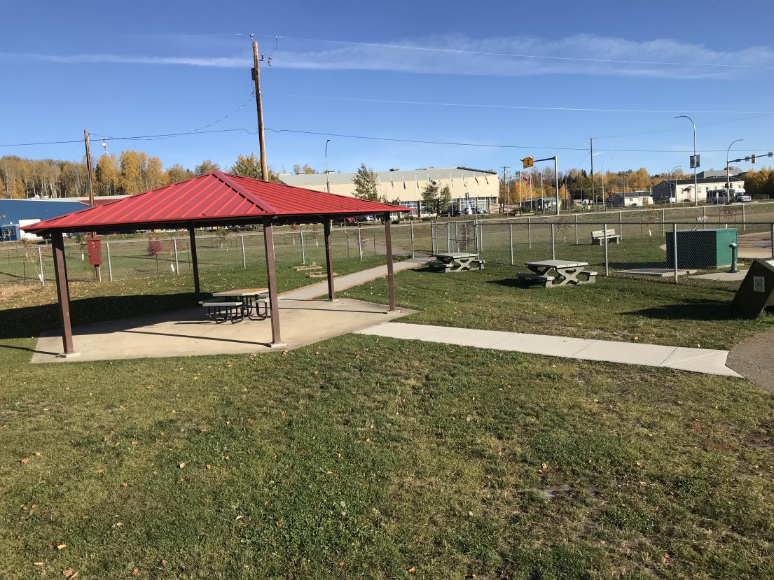 Park with red-roofed shelter and picnic tables on a sunny day.