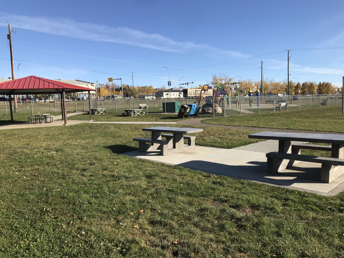 Park with picnic tables and a red-roofed shelter under a clear blue sky.
