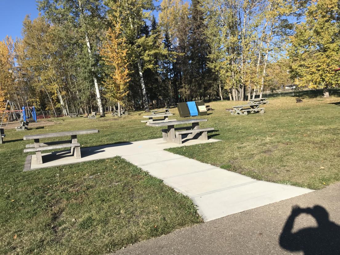 Park with picnic tables, pathway, and autumn trees under a clear blue sky.