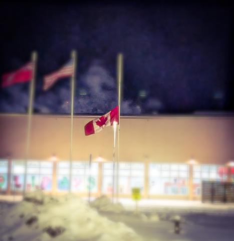 Canadian flag at half-mast, snowy night scene.