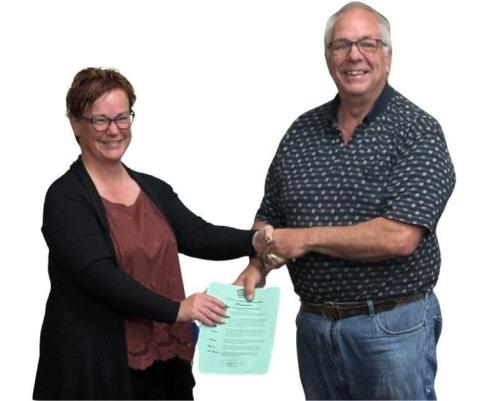 Two people smiling, shaking hands, one holding a document.