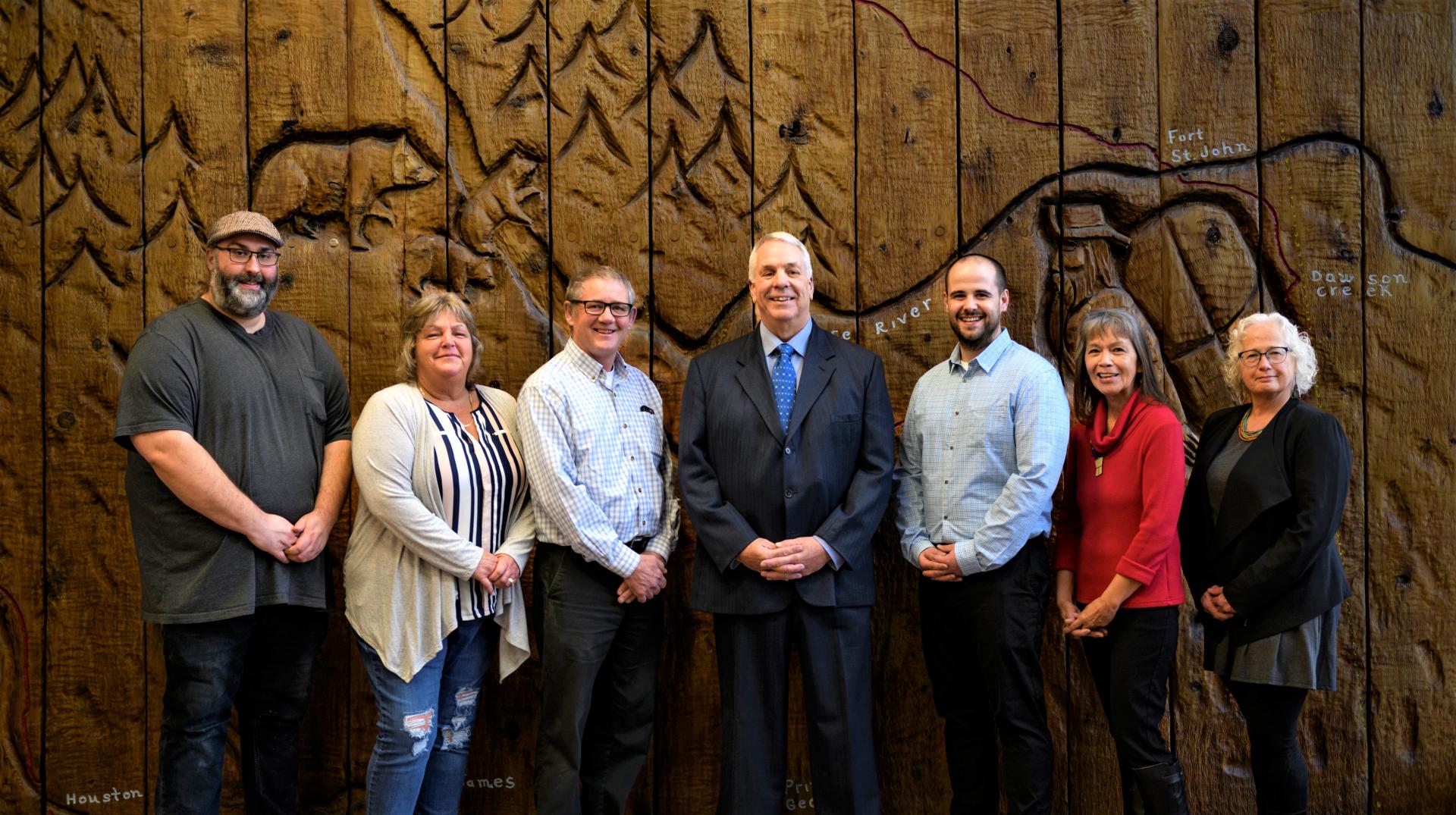 Seven people standing in front of a carved wooden mural.