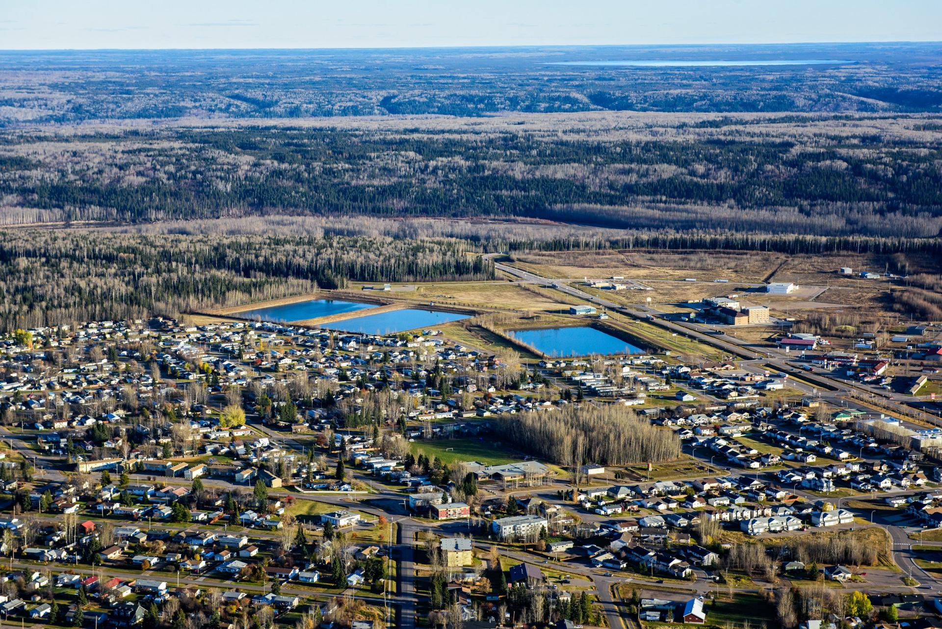 Aerial view of a town with scattered houses and two water bodies, surrounded by trees.